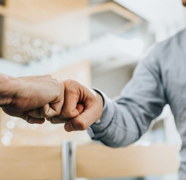 CLOSE UP OF TWO UNRECOGNIZABLE BUSINESSMEN GREETING EACH OTHER WITH FIST BUMP.