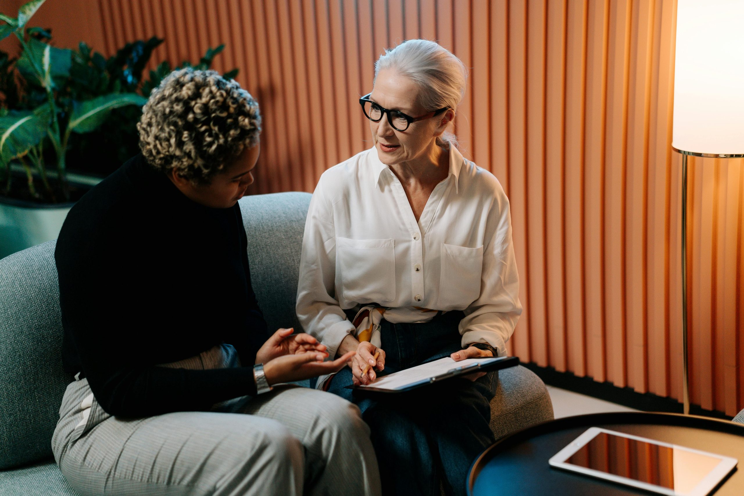 Two Professional Women Engaged In A Business Discussion Indoors With Documents.